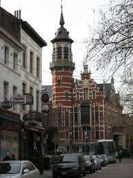 Plombier Jette sur fond de rue pavée typique, maisons en briques rouges et église Saint-Pierre en arrière-plan